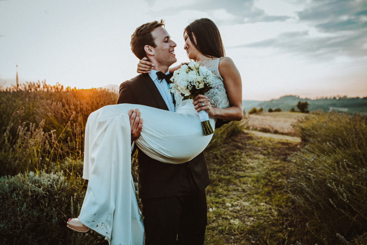 sposo prende in braccio sposa bellissima in un campo di lavanda